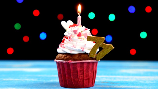 美味的生日蛋糕与燃烧的蜡烛和数字71在多色模糊的灯光背景视频素材