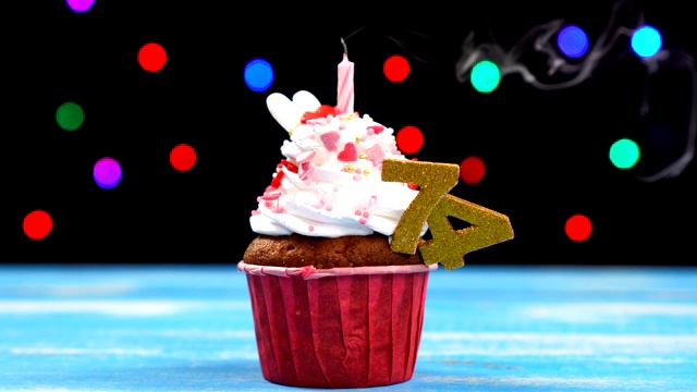 美味的生日蛋糕与燃烧的蜡烛和数字74在多色模糊的灯光背景视频素材
