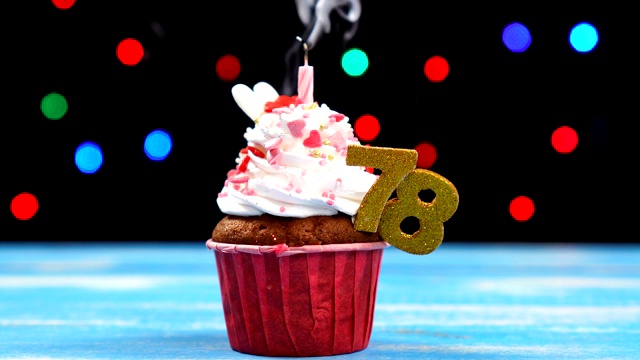 美味的生日蛋糕与燃烧的蜡烛和数字78在多色模糊的灯光背景视频素材