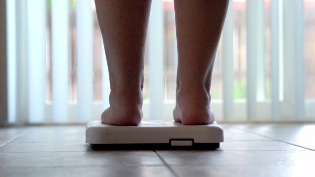 一个光着脚和腿的女人踩在浴室的秤上检查她的体重视频下载