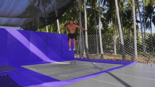 男子体操运动员在室外的蹦床上训练，背景是棕榈树。视频下载