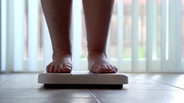 一个光着脚和腿的女人踩在浴室的秤上检查她的体重视频素材