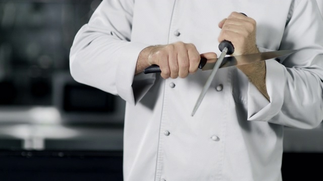 厨师用手磨刀的慢动作。近距离的手在厨房做饭。视频素材