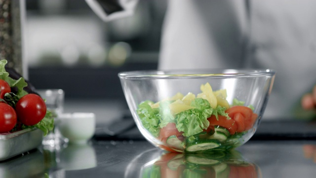 厨师在厨房餐厅给沙拉加盐。用手腌制蔬菜的特写。视频素材