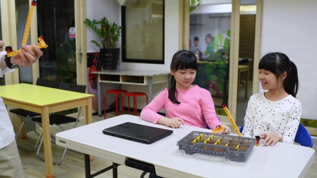 镜头从两个正在制作机器人的小孩移到另一张桌子上，在那里，两个小女孩正在制作起重机视频素材