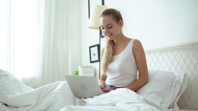 微笑的女人躺在床上用笔记本电脑视频素材