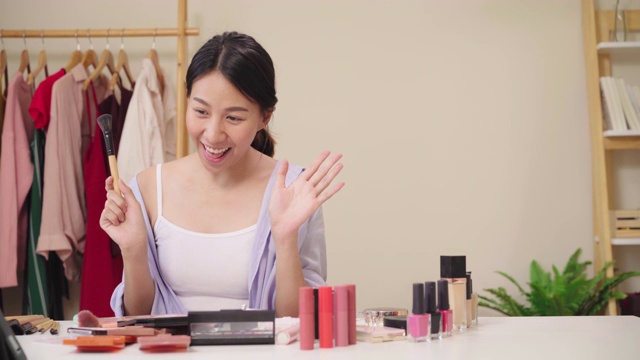 美妆博主坐在写字板前拍摄美妆视频。快乐美丽的年轻亚洲女子用化妆品点评化妆教程在社交网络直播。视频素材