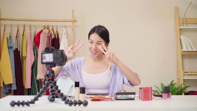 美妆博主坐在镜头前拍摄美妆视频。快乐美丽的年轻亚洲女子用化妆品点评化妆教程在社交网络直播。视频购买