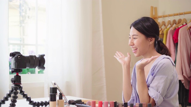 美妆博主坐在镜头前拍摄美妆视频。快乐美丽的年轻亚洲女子用化妆品点评化妆教程在社交网络直播。视频素材
