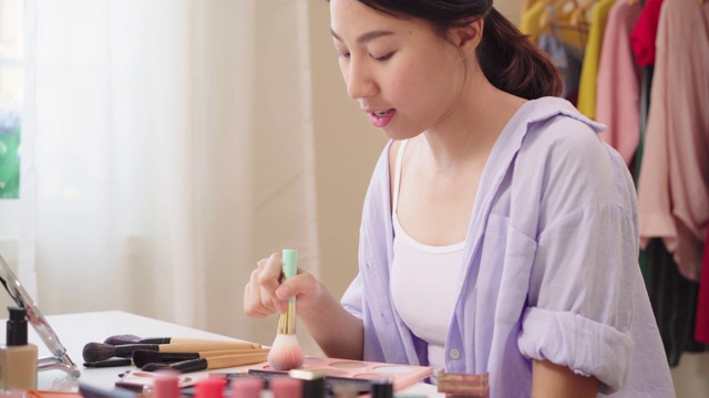 美妆博主坐在镜头前拍摄美妆视频。快乐美丽的年轻亚洲女子用化妆品点评化妆教程在社交网络直播。视频素材