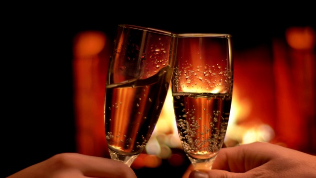 一对相爱的夫妇的双手的特写镜头碰杯满香槟庆祝一个晚上的约会与舒适温暖的壁炉在室内的背景视频下载