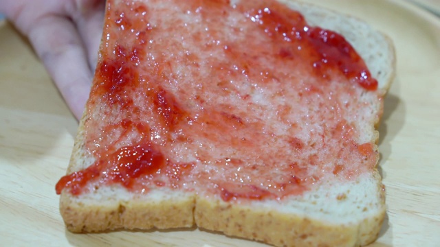 近了，女人拿着刀在面包上抹果酱草莓。视频下载