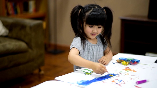 可爱的小女孩在家里沙发前的桌子上用彩绘纸创作艺术。教育的概念。视频下载
