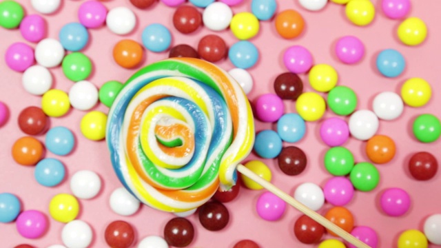 五颜六色的棒棒糖和不同颜色的圆糖。俯视图粉色粉彩背景视频下载