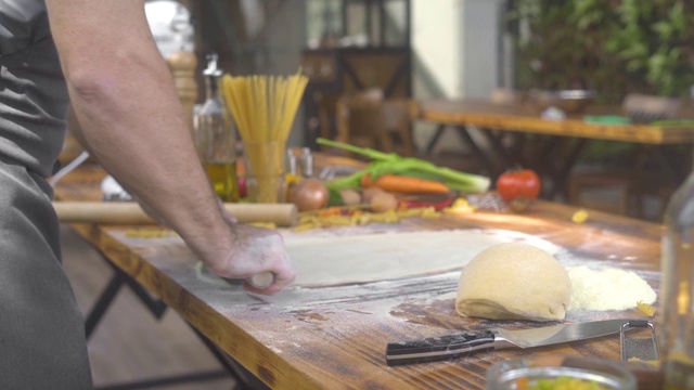 一名男子在厨房的桌子上为意大利面滚动新鲜的面团。厨师用擀面杖擀薄饼。自制糕点、蛋糕、披萨和意大利面。做手工制作的食物视频素材