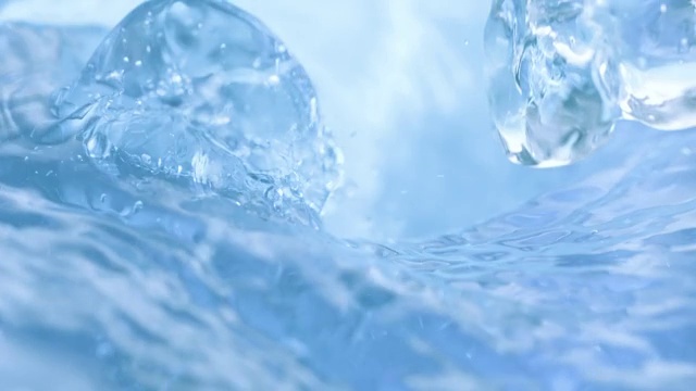 三个冰块落入旋转的浅蓝色的水中，溅起水花，特写慢镜头。视频素材