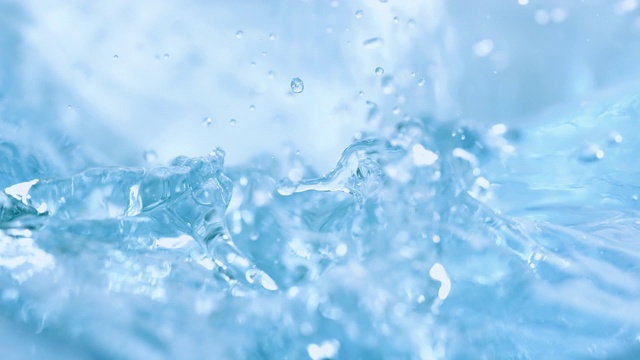 三个冰块落入旋转的浅蓝色的水中，溅起水花，特写慢镜头。视频素材