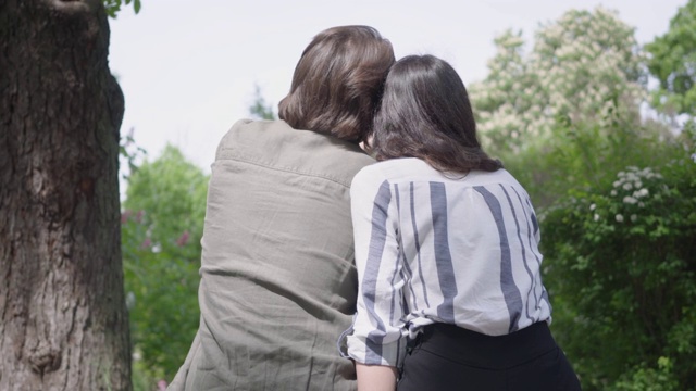一个年轻漂亮的夫妇在休闲衣服花时间一起在公园的背影。视频下载