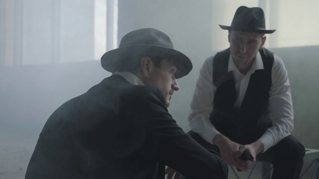 两个戴着帽子的时髦男人坐在一幢废弃的大楼里讨论生意。视频素材