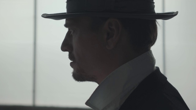 一个英俊自信的男人在大窗户前戴着一顶帽子的肖像。视频素材