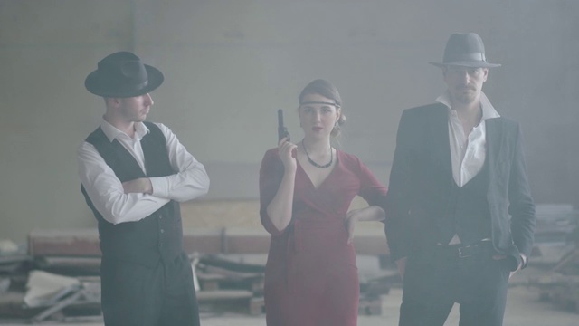 在一座废弃的建筑里，两个戴着帽子、穿着西装的男人和一个穿红色裙子的女人走向摄像机。视频素材