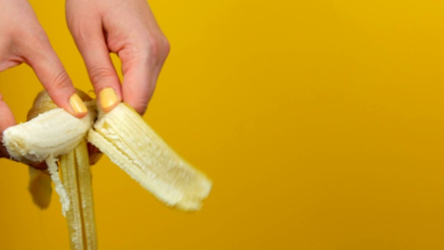 女人的手在黄色的背景上剥一个成熟的香蕉果实的皮视频素材