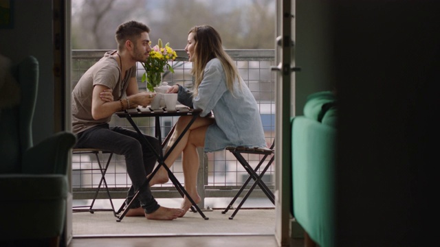 年轻夫妇在阳台上喝着早茶聊天并分享一个亲密的吻。视频下载