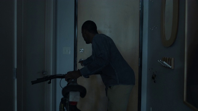 一个年轻的非洲裔美国人拿着他的钥匙，骑着自行车走出了他的城市公寓。视频素材