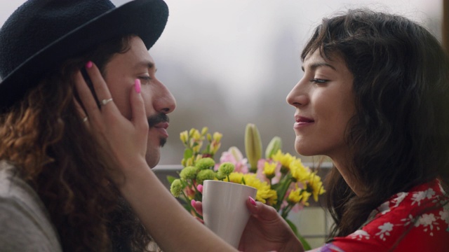 一对相爱的年轻情侣在阳台上享受着早晨一杯茶，分享着几个亲密的吻。视频下载