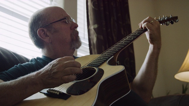 一名五十多岁的白人男子在客厅里弹原声吉他视频素材