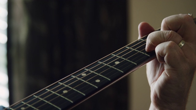 一个白人男子的手指在室内演奏音乐的时候压在一个原声吉他的指板上的特写视频素材