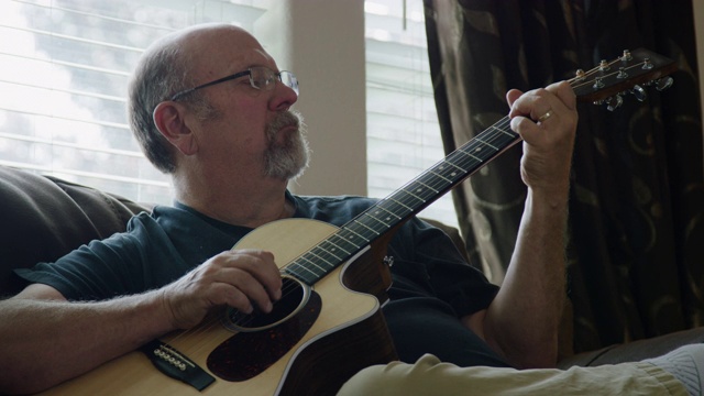 一名五十多岁的白人男子在客厅里弹原声吉他视频素材