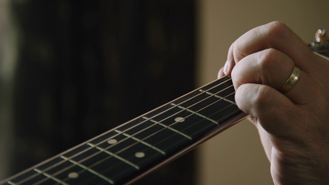 一个白人男子的手指在室内演奏音乐的时候压在一个原声吉他的指板上的特写视频素材