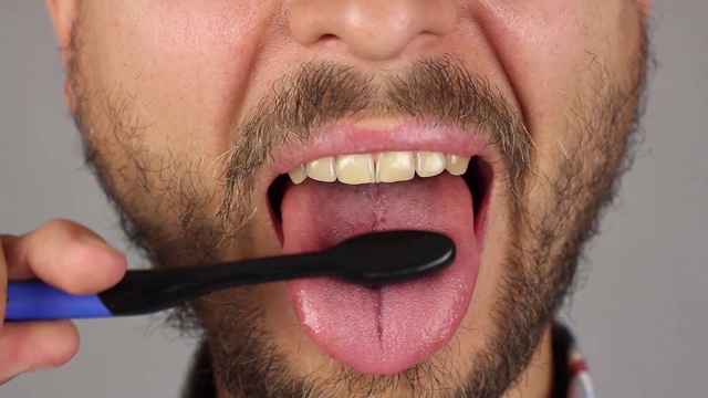 有胡子的男人用黑色的牙刷彻底刷他的舌头，正面，按摩和清洁牙斑，特写视频下载