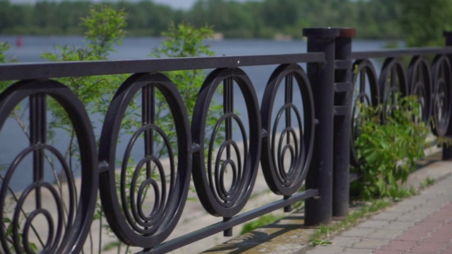 在一个阳光明媚的夏日，城市公园的路堤上有黑色金属的砖元素装饰围栏和绿色植物。特写镜头。摄像机沿着栅栏移动视频下载