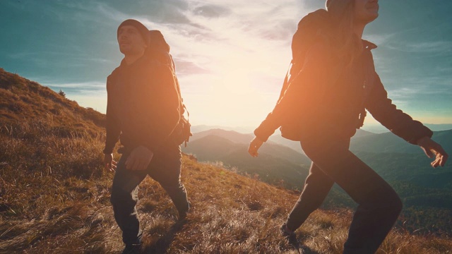 这对夫妇在夕阳的背景下走在山上。慢动作视频素材
