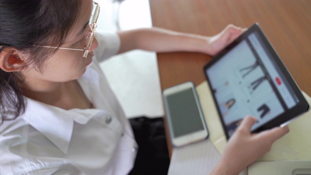 亚洲大学生女孩读书，工作和网上购物与笔记本电脑和智能手机在公共图书馆做她的家庭作业视频下载