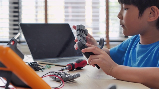 男孩在家里用电脑制作和编程，并制作一个机器人手臂作为学校的科学项目。他对自己的工作非常满意。教育、儿童、技术、科学是人们的理念视频素材
