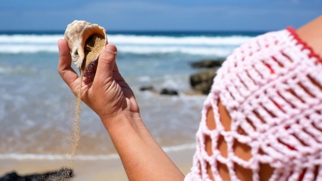 美丽的白人妇女的特写镜头从背后抱着一个小的白色贝壳满沙子落在地上-假日苏美尔假期自由的概念与美丽的自然户外-海在背景的旅游和旅游主题视频下载