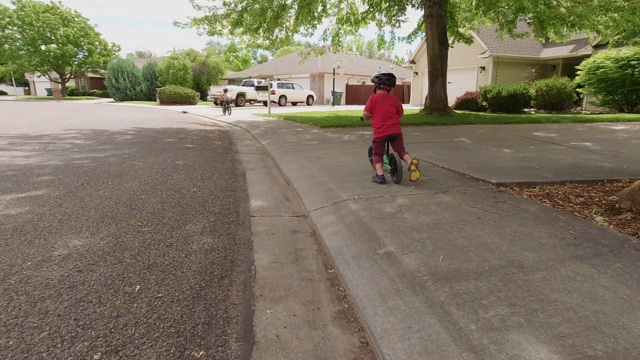 一个四岁的白人男孩戴着头盔，和他的哥哥在一个多云的天空下的住宅区骑他的平衡自行车视频素材