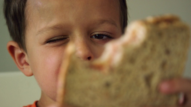 一个可爱的6岁白人男孩向镜头展示了他的三明治上的咬痕，然后又咬了一口，笑了视频下载