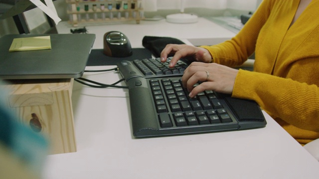 一位三十多岁的白人妇女在她的键盘上打字，因为她在一个家庭办公室室内工作，以缝纫材料为背景视频素材