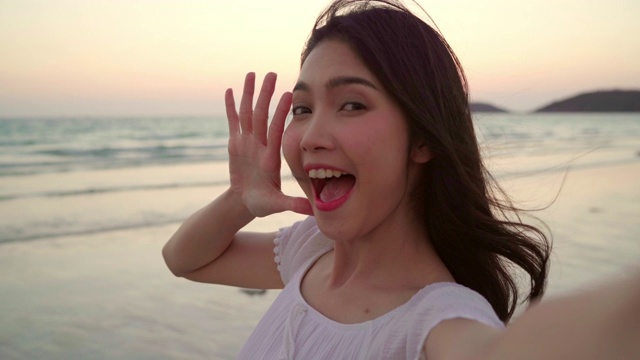 游客亚洲女人在海滩自拍，年轻美丽的女性开心的微笑用手机在海滩附近的海边当日落在晚上自拍。生活方式女性旅行海滩概念。视频下载