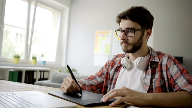 英俊年轻的平面设计师工作在家庭办公室使用图形平板电脑和笔记本电脑视频下载