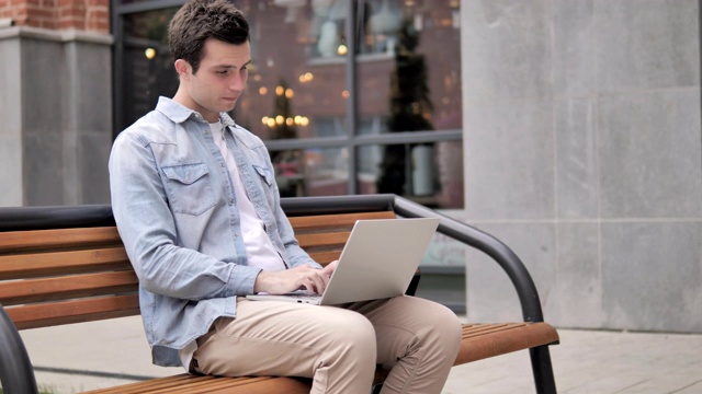 一名年轻人在户外使用笔记本电脑时颈部疼痛视频素材