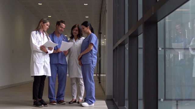 一群医生和护士在医院走廊上讨论一些东西，同时看着文书工作微笑视频素材