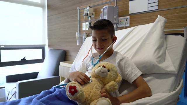 可爱的住院小男孩正在用听诊器检查他的泰迪熊的心脏视频素材