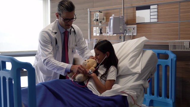 好玩的男儿科医生在住院的小女孩的帮助下听泰迪熊的心跳视频素材