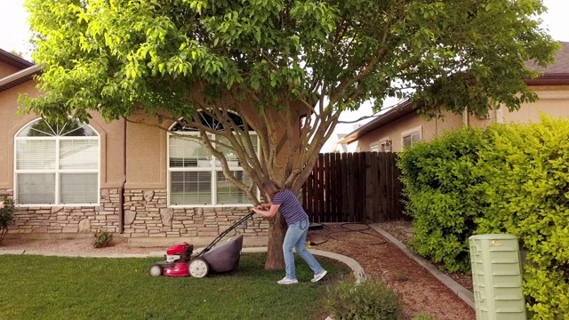 一个中年妇女在修剪草坪，享受仲春天气的无人机视频剪辑视频下载