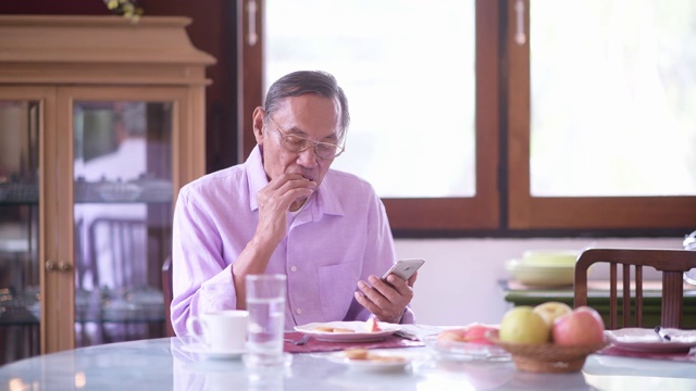 用智能手机在家吃水果的亚洲老人视频素材